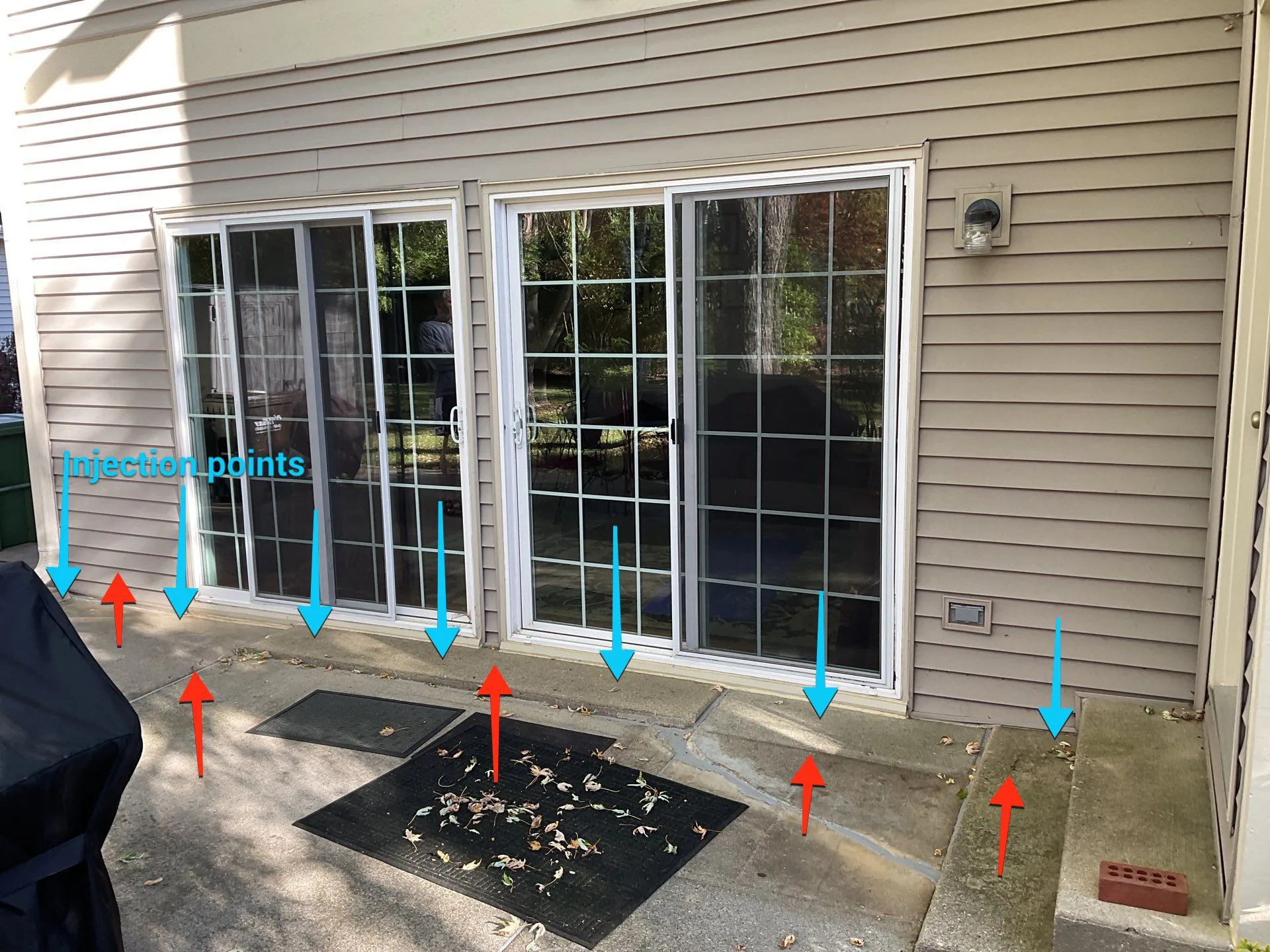Concrete patio and foundation area marked with blue and red arrows indicating uneven settlement patterns and soil injection evaluation points during a professional foundation assessment.