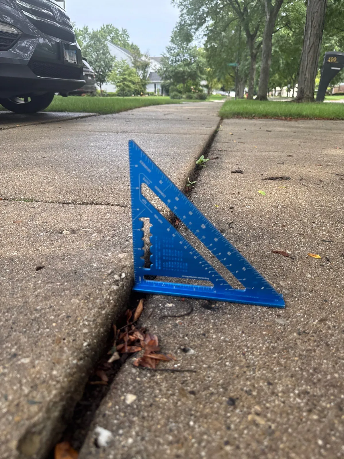 Close-up detail of sunken concrete showing a significant gap between two concrete slabs measured with a blue triangle level tool, demonstrating the uneven settlement caused by soil instability beneath the surface.