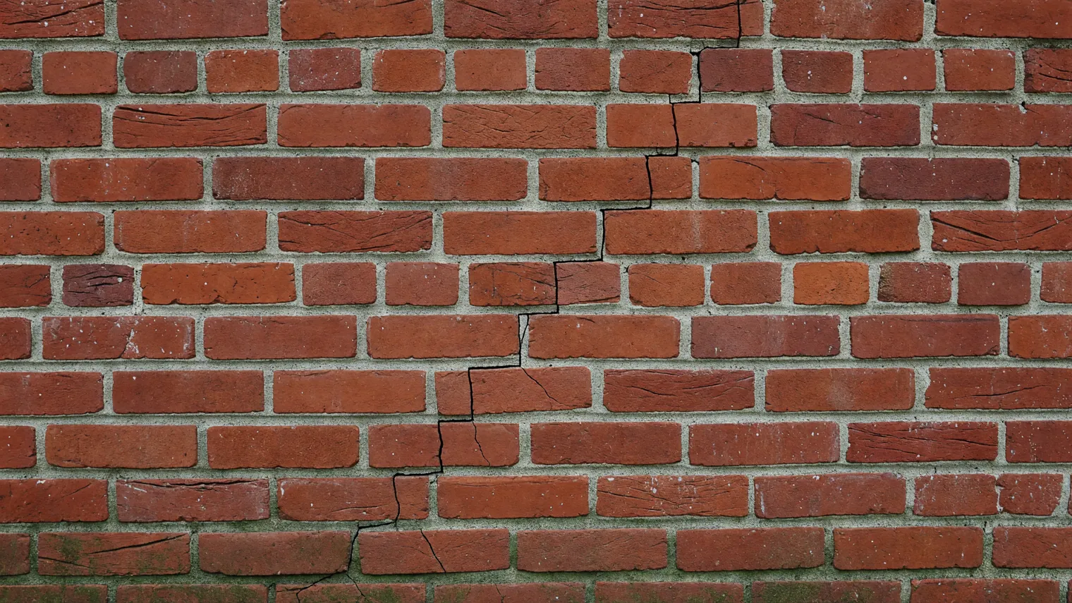 A red brick wall with a stair-step crack climbing diagonally through the mortar joints, a pattern often linked to foundation movement.
